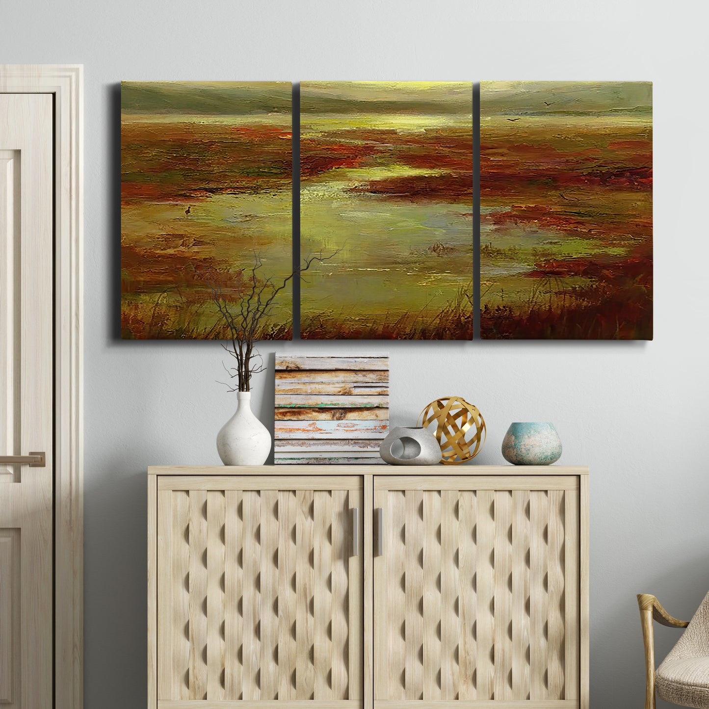Three-panel canvas wall art featuring coastal shoreline with warm light, displayed above a cabinet in an entryway.