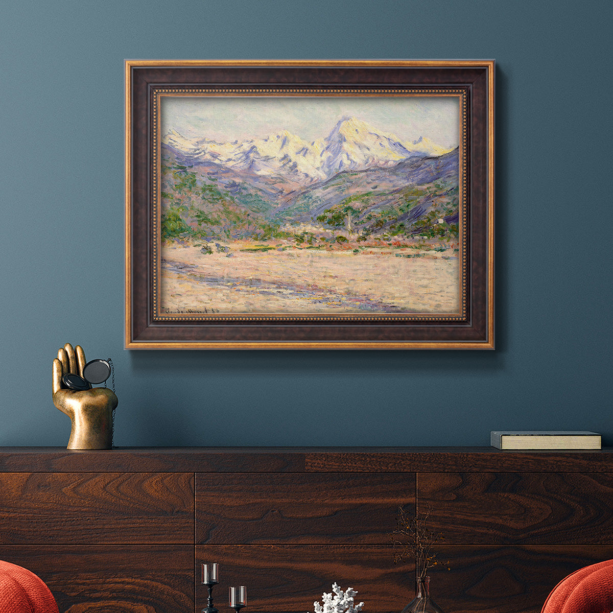 Impressionist valley landscape in southern France by Claude Monet in an ornate bronzed mahogany wood frame displayed in a dark-toned interior setting.