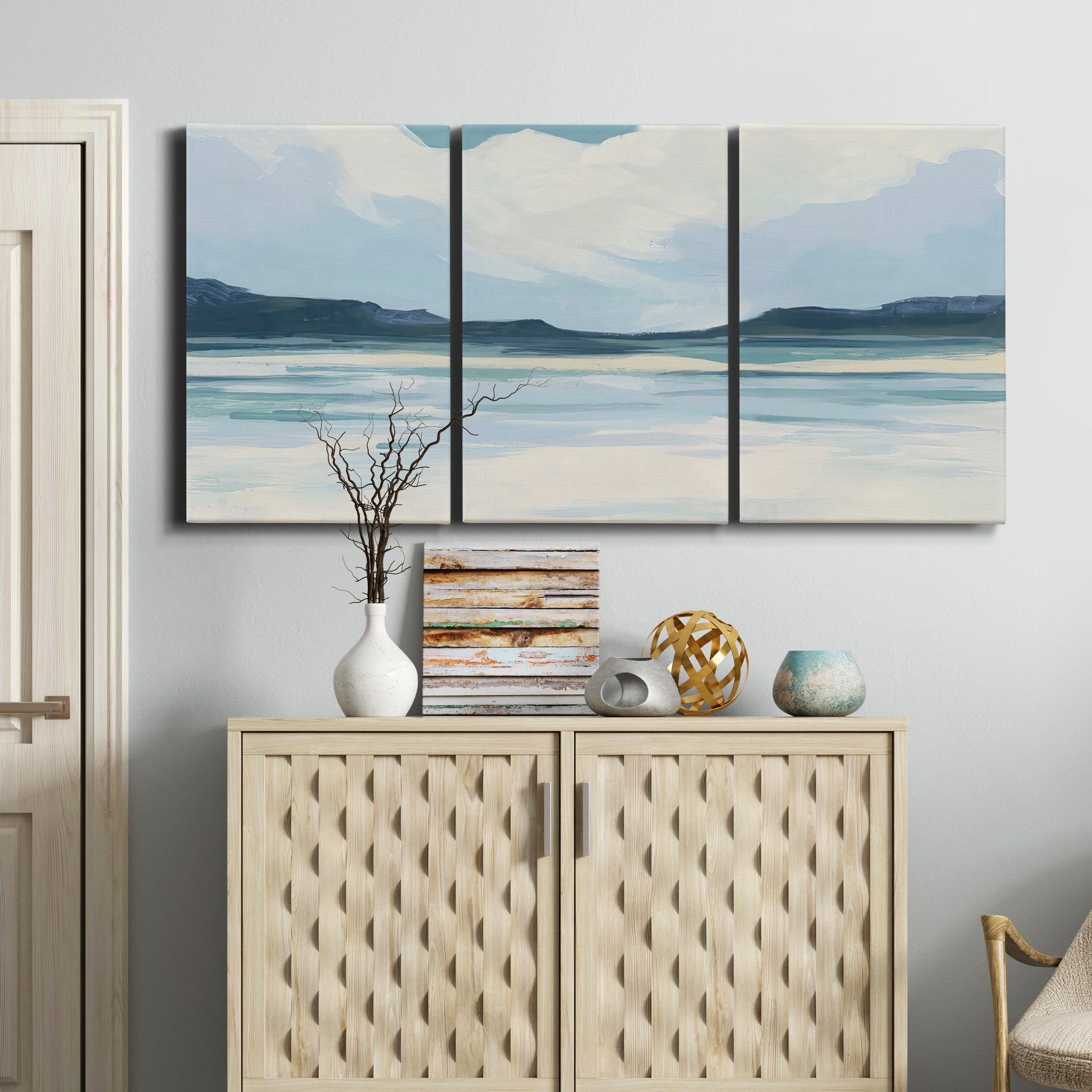Three-panel canvas wall art featuring soft coastal shoreline landscape, displayed above a cabinet in an entryway.
