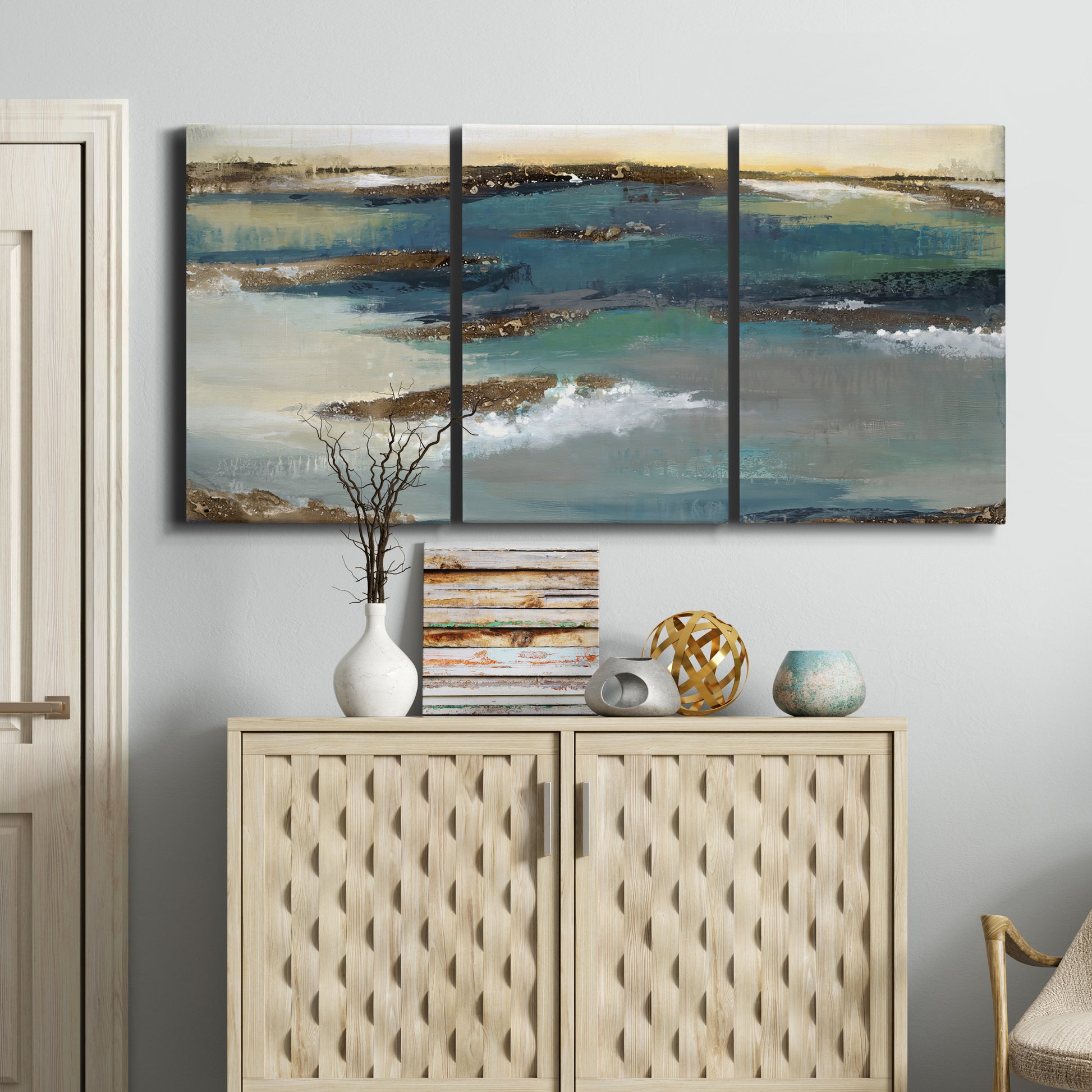 Three-panel canvas wall art featuring rocky coastal bluff above sea, displayed above a cabinet in an entryway.