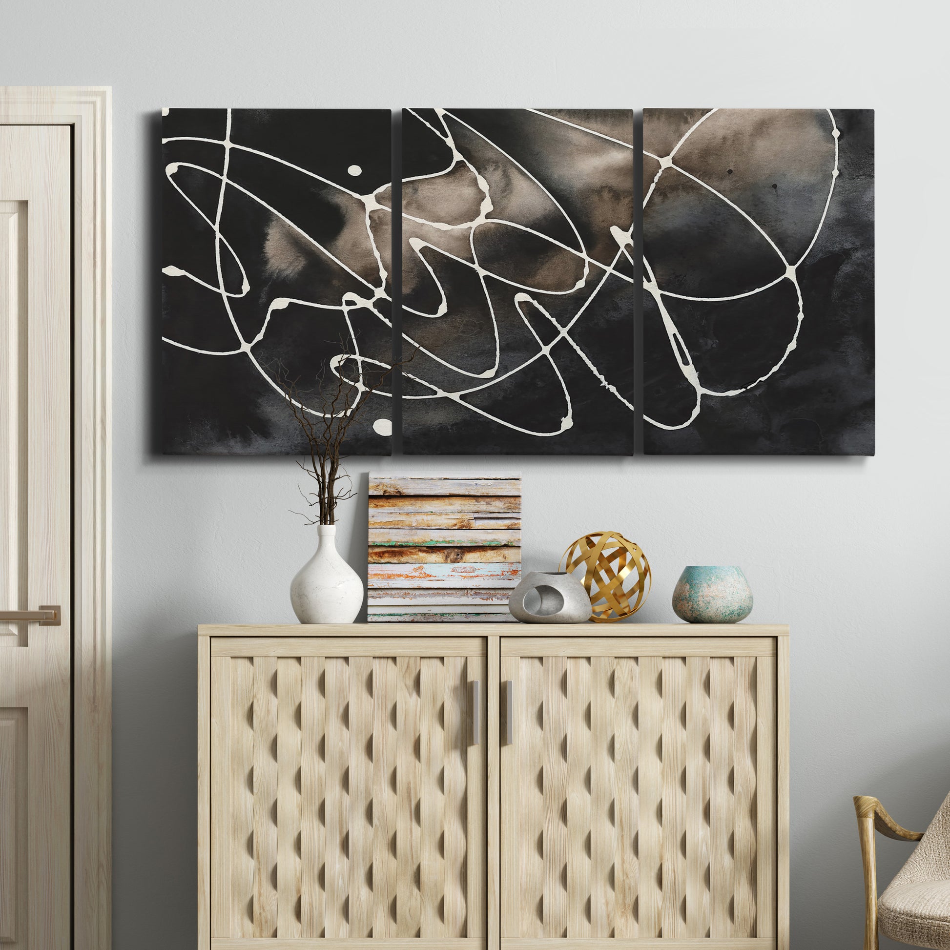 Three-panel canvas wall art featuring dark swirling abstract motion, displayed above a cabinet in an entryway.