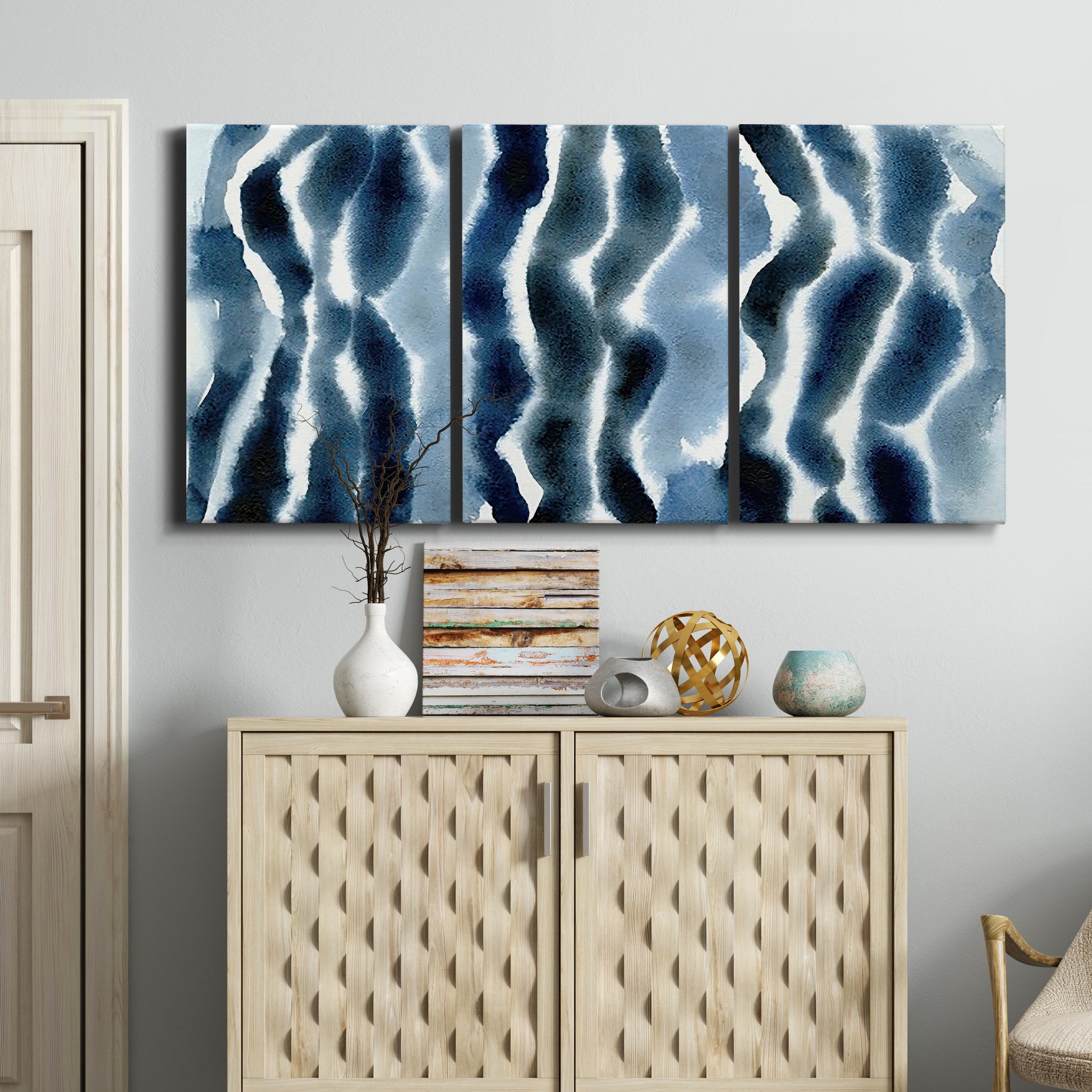 Three-panel canvas wall art featuring flowing blue watercolor wave forms, displayed above a cabinet in an entryway.