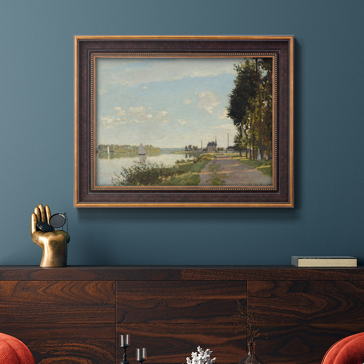 Impressionist river scene with red boats by Claude Monet in an ornate bronzed mahogany wood frame displayed in a dark-toned interior setting.