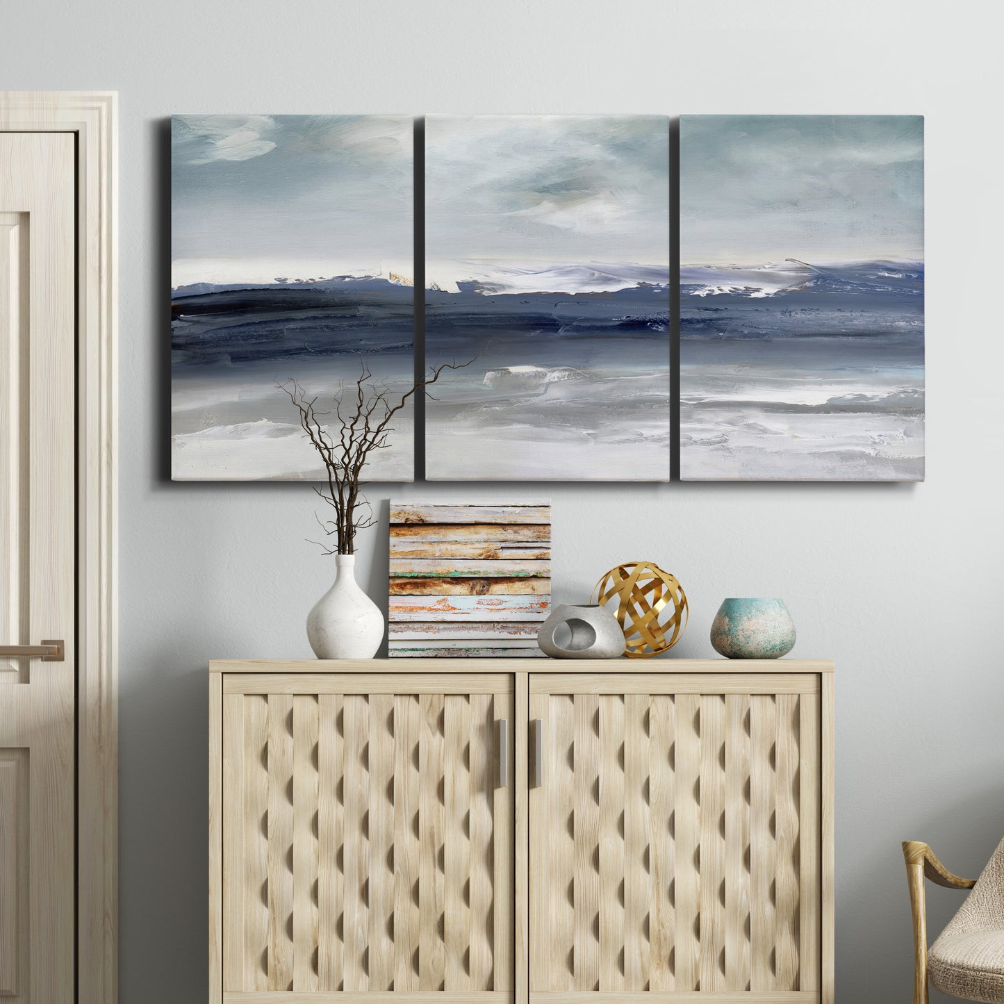 Three-panel canvas wall art featuring abstract coastal tones and movement, displayed above a cabinet in an entryway.