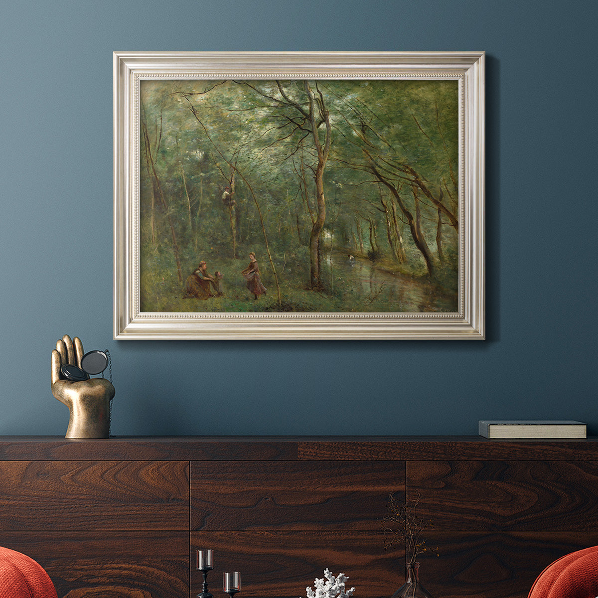 Traditional rural landscape scene with figures by Jean-Baptiste-Camille Corot in an ornate champagne frame displayed in a dark-toned interior setting.