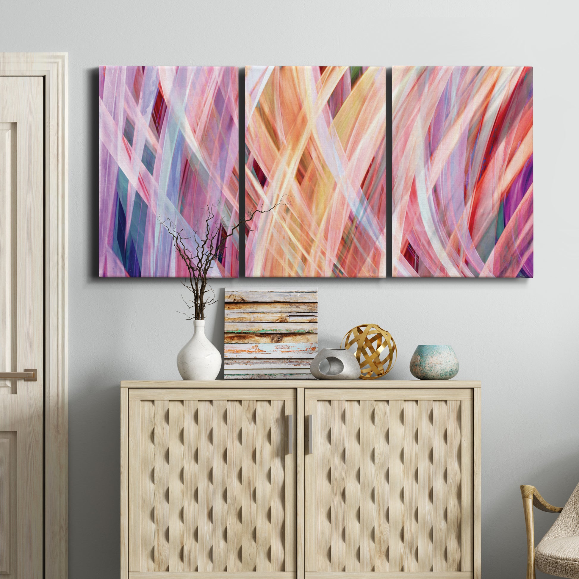 Three-panel canvas wall art featuring layered modern abstract color ribbons, displayed above a cabinet in an entryway.