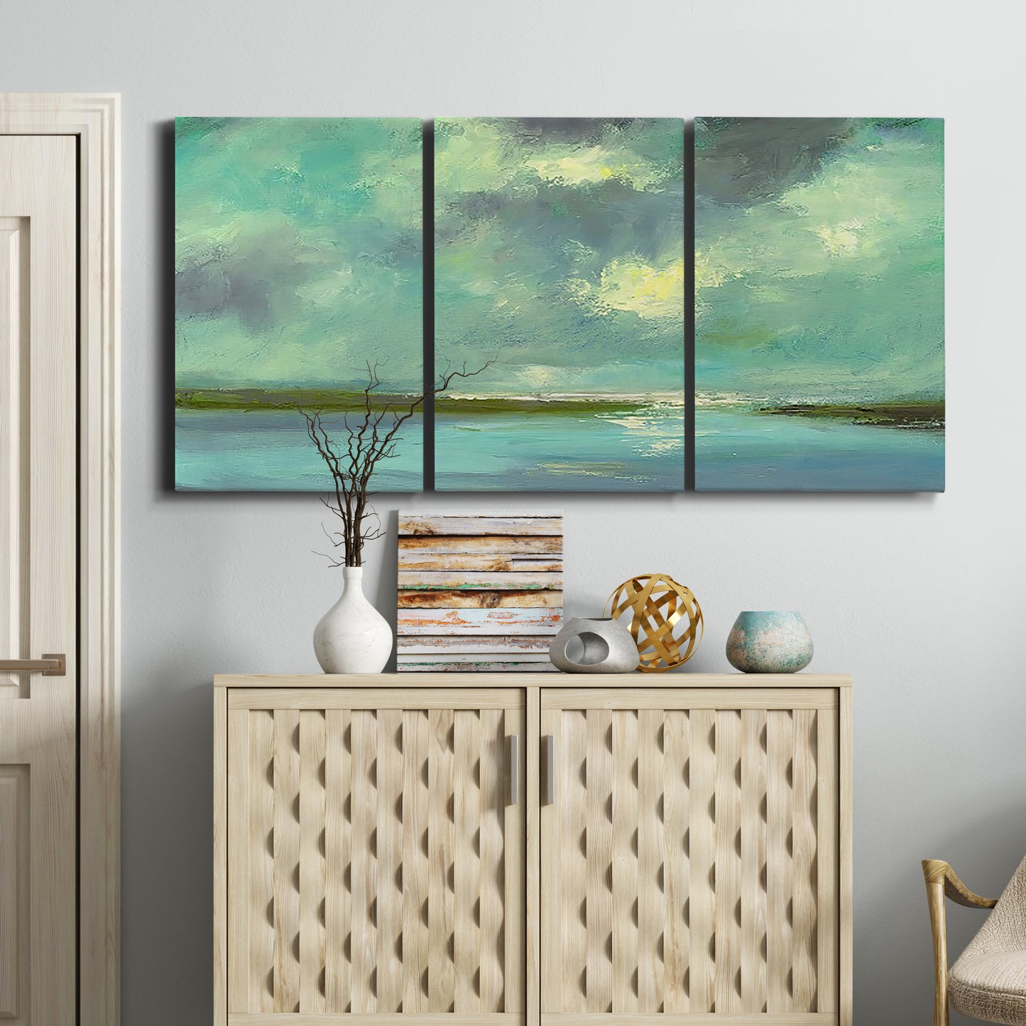 Three-panel canvas wall art featuring still lagoon water beneath open sky, displayed above a cabinet in an entryway.