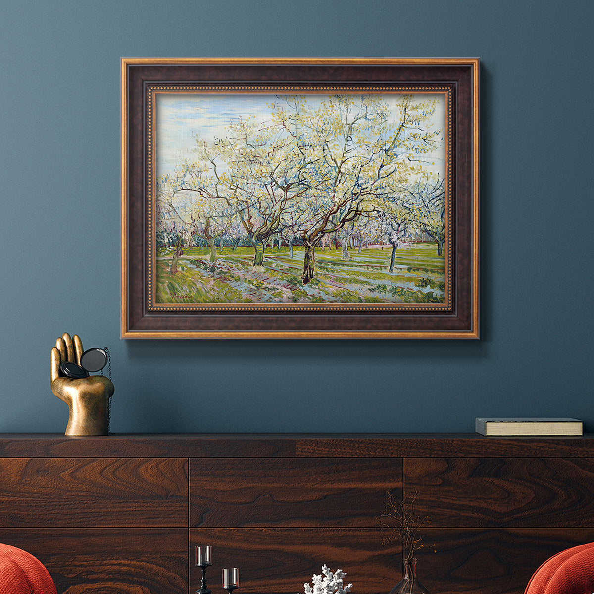 Impressionist white-blossomed orchard landscape by Vincent van Gogh in an ornate bronzed mahogany wood frame displayed in a dark-toned interior setting.