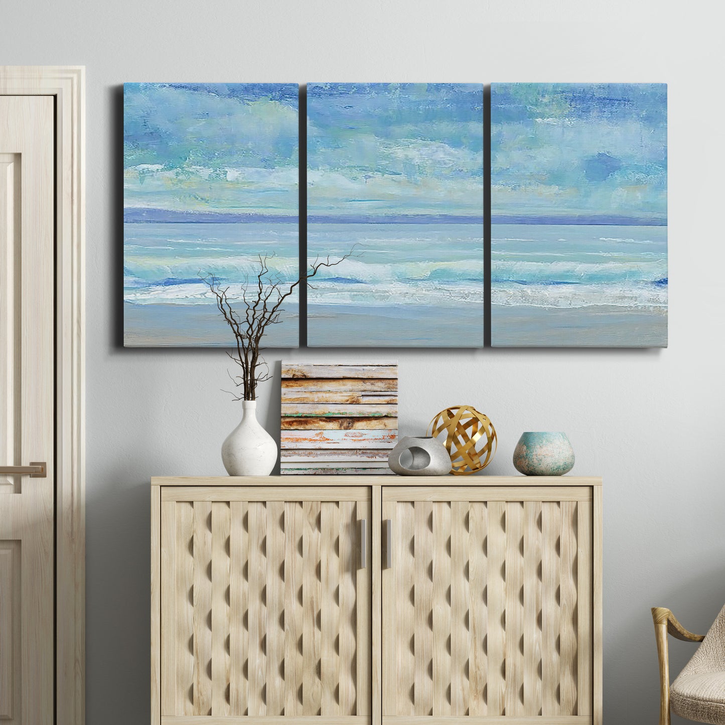 Three-panel canvas wall art featuring rolling ocean surf along shoreline, displayed above a cabinet in an entryway.