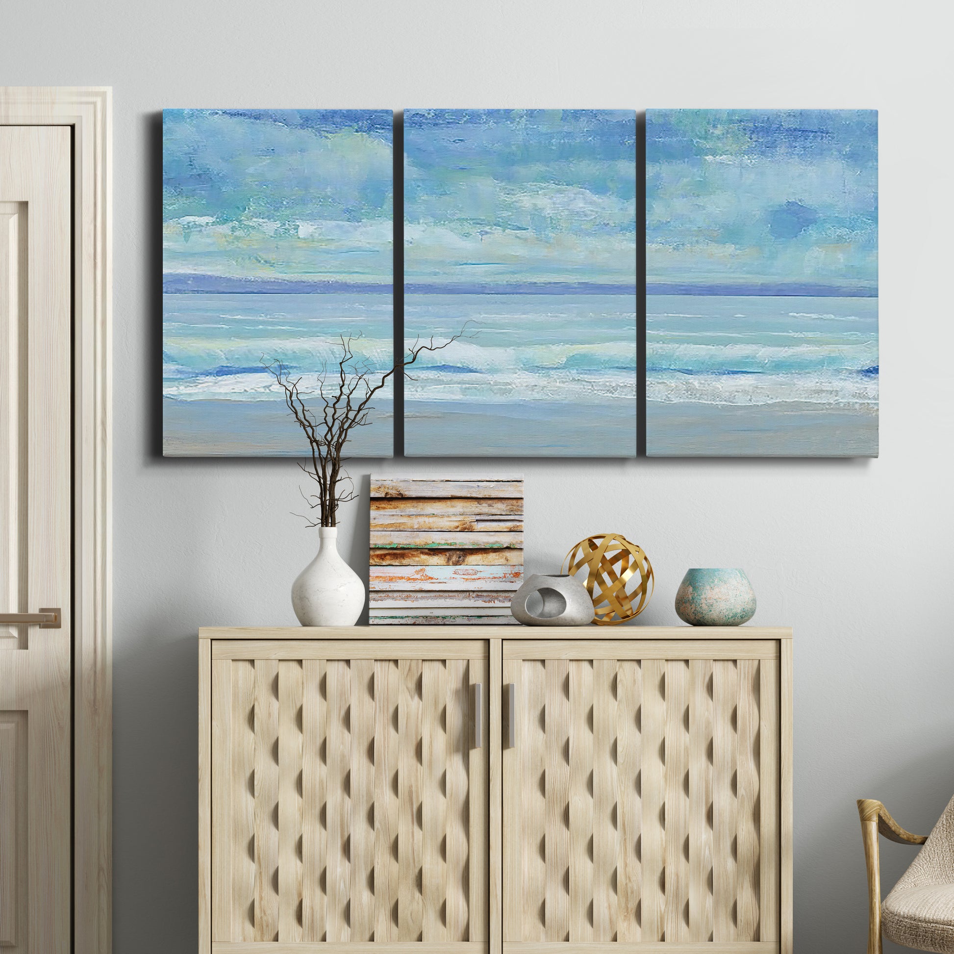 Three-panel canvas wall art featuring rolling ocean surf along shoreline, displayed above a cabinet in an entryway.
