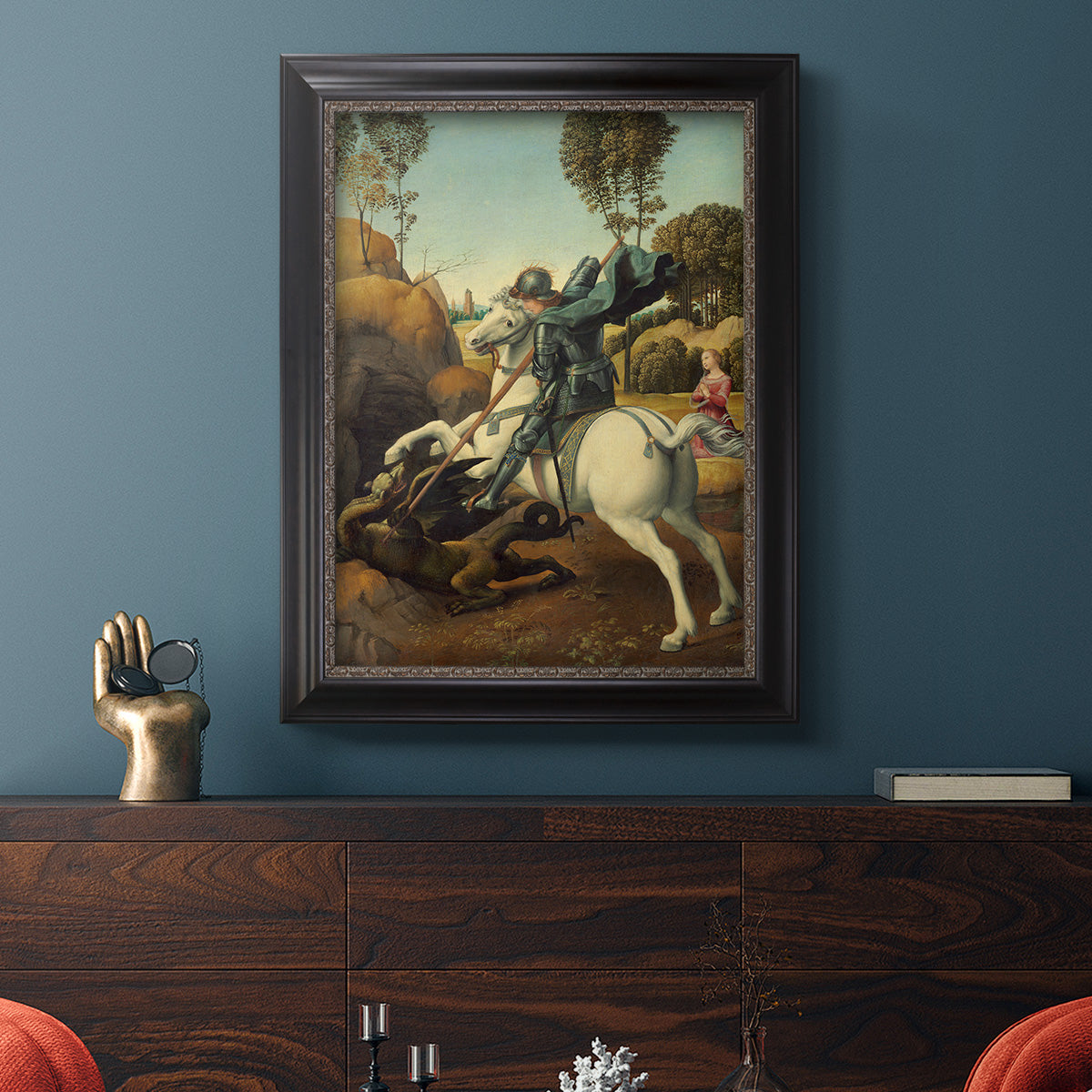 Religious painting of Saint George slaying the dragon by Raphael in an ornate black frame with gilded inner detail displayed in a dark-toned interior setting.
