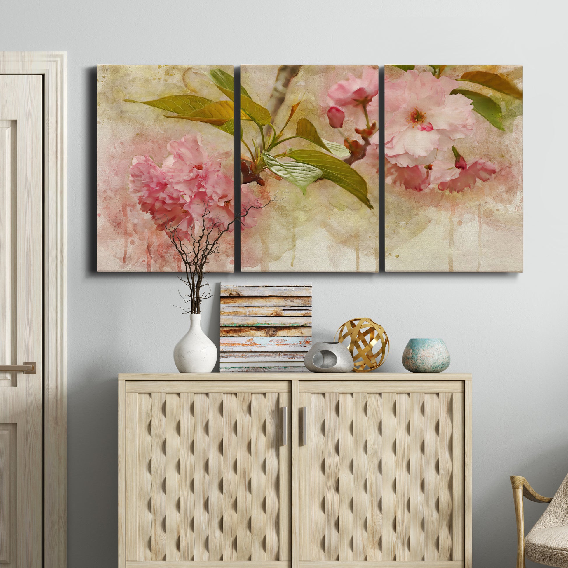 Three-panel canvas wall art featuring soft floral blossom composition, displayed above a cabinet in an entryway.