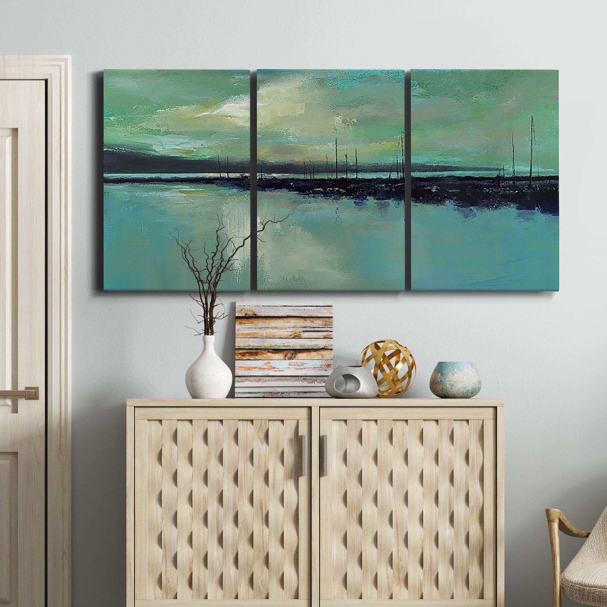 Three-panel canvas wall art featuring calm harbor water with glowing horizon, displayed above a cabinet in an entryway.