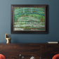 Impressionist garden scene with Japanese bridge and water lilies by Claude Monet in an ornate black frame with gilded inner detail displayed in a dark-toned interior setting.