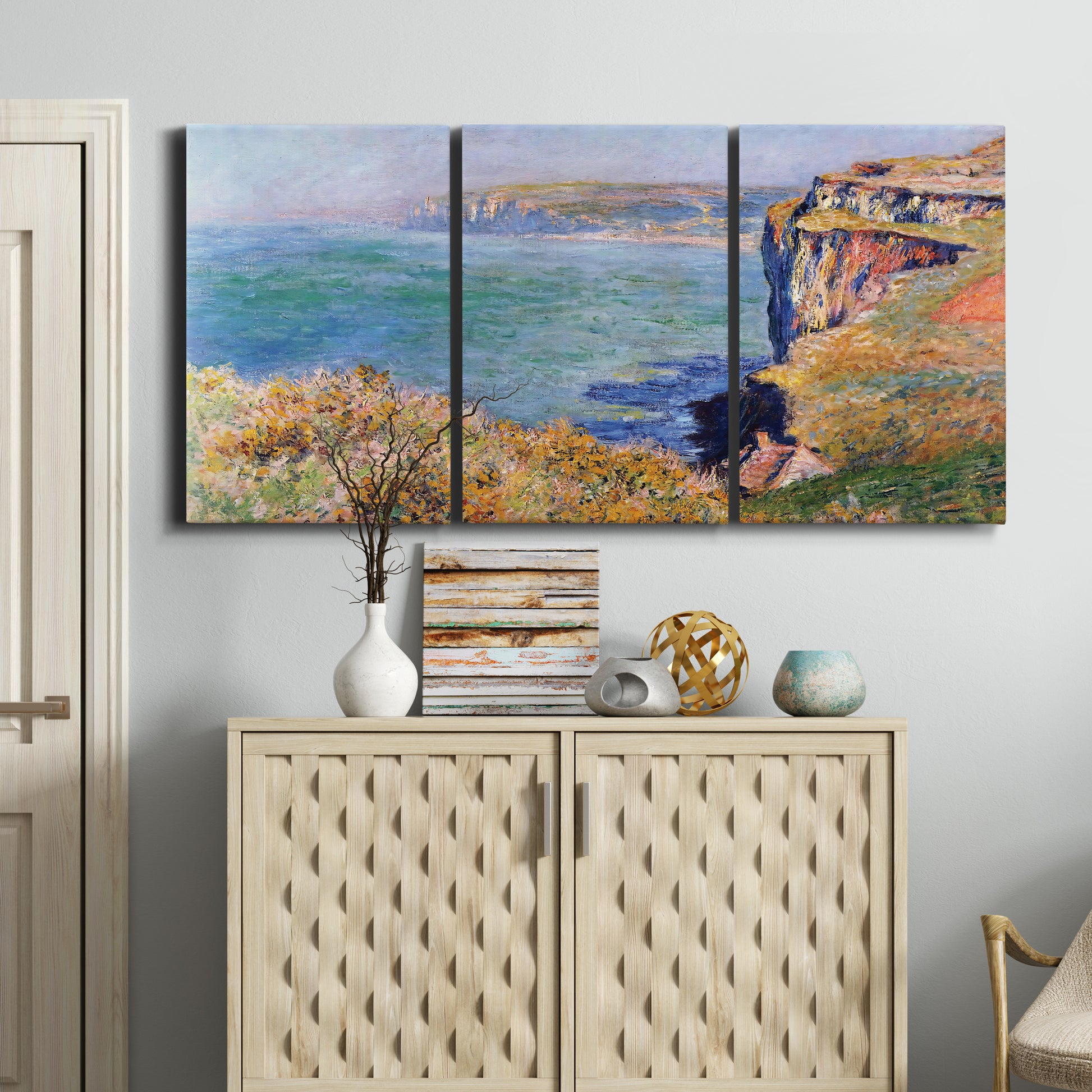 Three-panel canvas wall art featuring coastal village view near dieppe, displayed above a cabinet in an entryway.