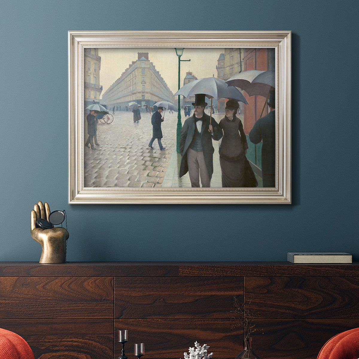 Impressionist urban street scene in the rain by Gustave Caillebotte in an ornate champagne frame displayed in a dark-toned interior setting.