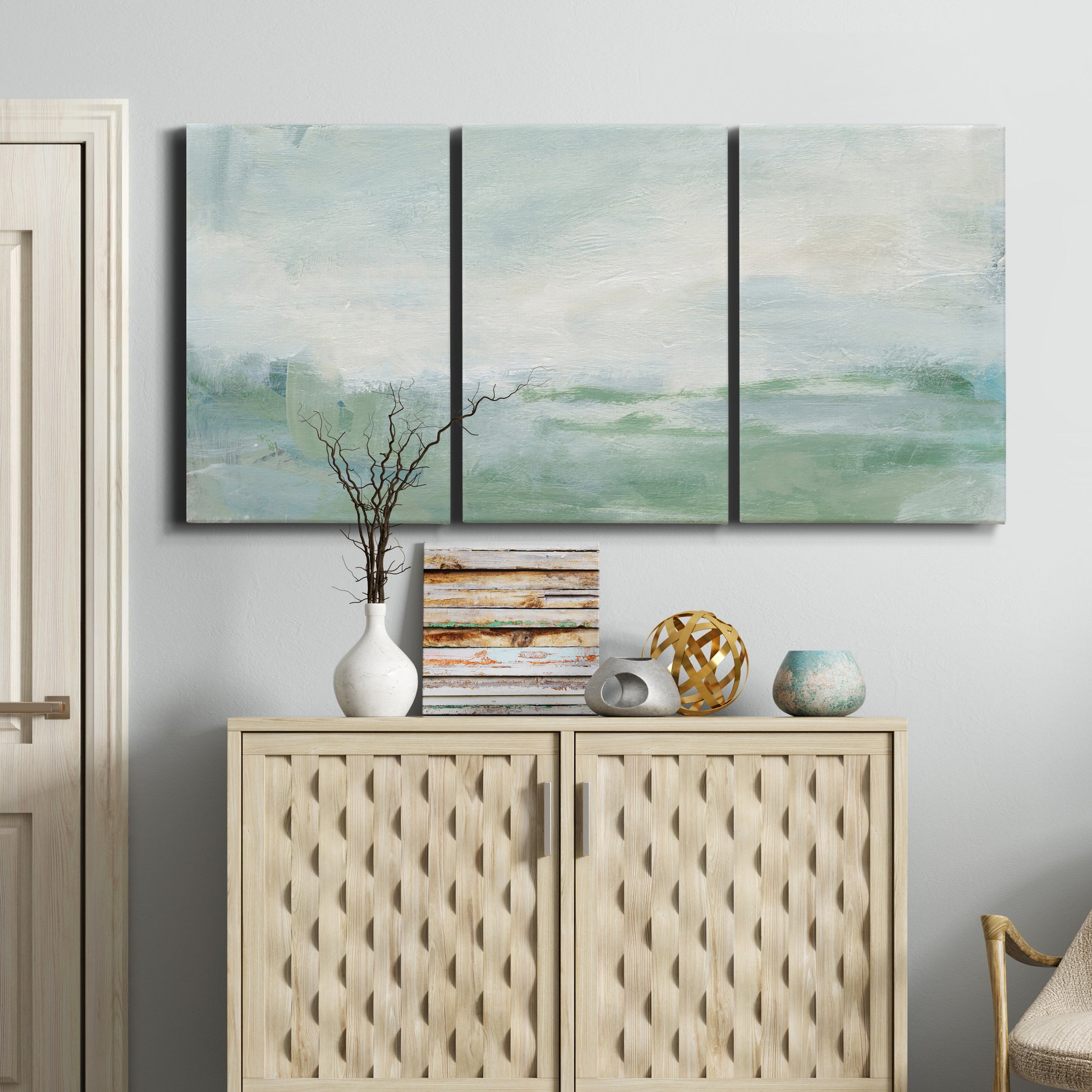 Three-panel canvas wall art featuring soft abstract coastal tones, displayed above a cabinet in an entryway.