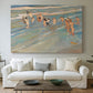 Canvas art print detailing a coastal scene with children and reflective shoreline, centered above a sofa as a large focal wall piece