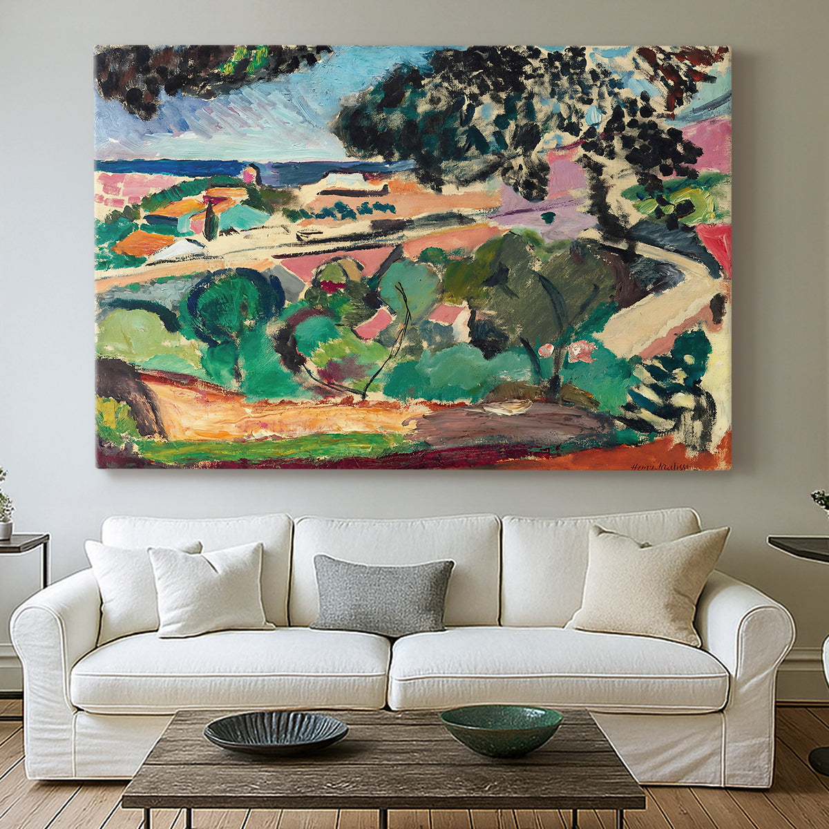 Canvas art print detailing a stylized coastal landscape with buildings and trees, centered above a sofa as a large focal wall piece