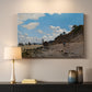 Canvas art print detailing a coastal landscape with boats and people along shore, mounted in a softly lit interior space