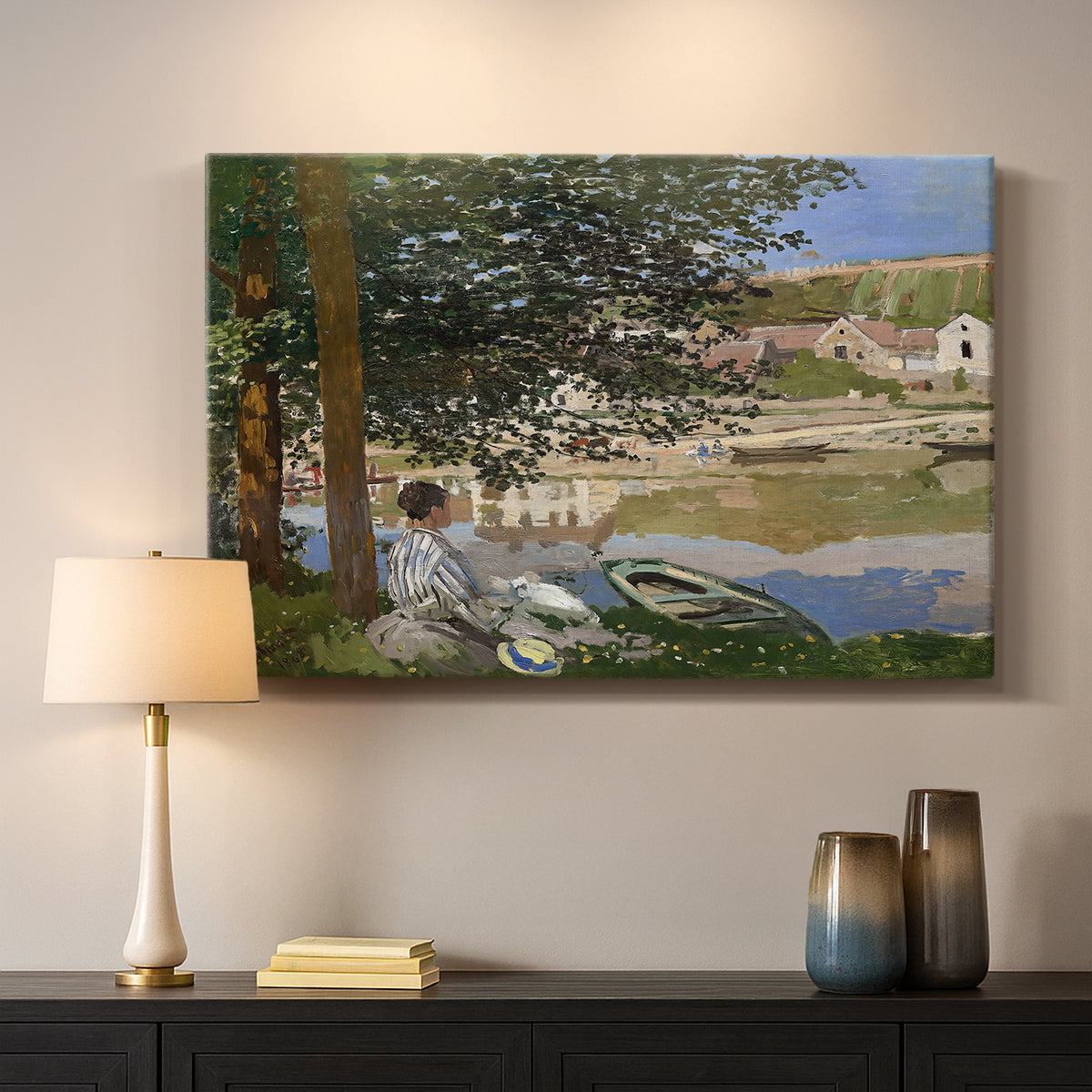 Canvas art print detailing a quiet outdoor setting with figures near river under foliage, mounted in a softly lit interior space