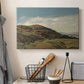 Canvas art print detailing a peaceful rural vista with greenery, water, and architectural landmark, displayed in a softly lit workspace setting