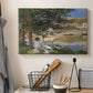 Canvas art print detailing a quiet outdoor setting with figures near river under foliage, displayed in a softly lit workspace setting