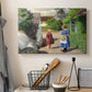 Canvas art print detailing a peaceful summer day with figures in small town environment, displayed in a softly lit workspace setting