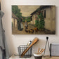 Canvas art print detailing a countryside visit scene with figures in front of rustic buildings, displayed in a softly lit workspace setting