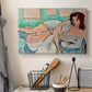 Canvas art print detailing a stylized female figure in a relaxed pose with drapery, displayed in a softly lit workspace setting