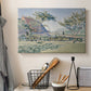 Canvas art print detailing a landscape with village and meadow, displayed in a softly lit workspace setting