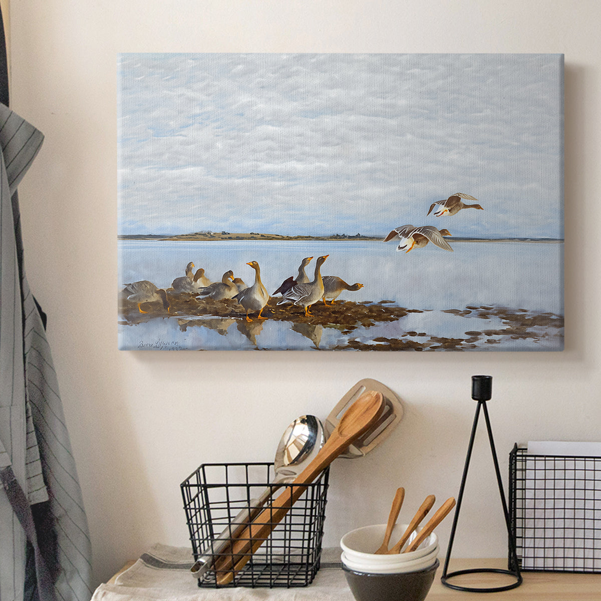 Canvas art print detailing a flock of geese positioned along marshy terrain, displayed in a softly lit workspace setting