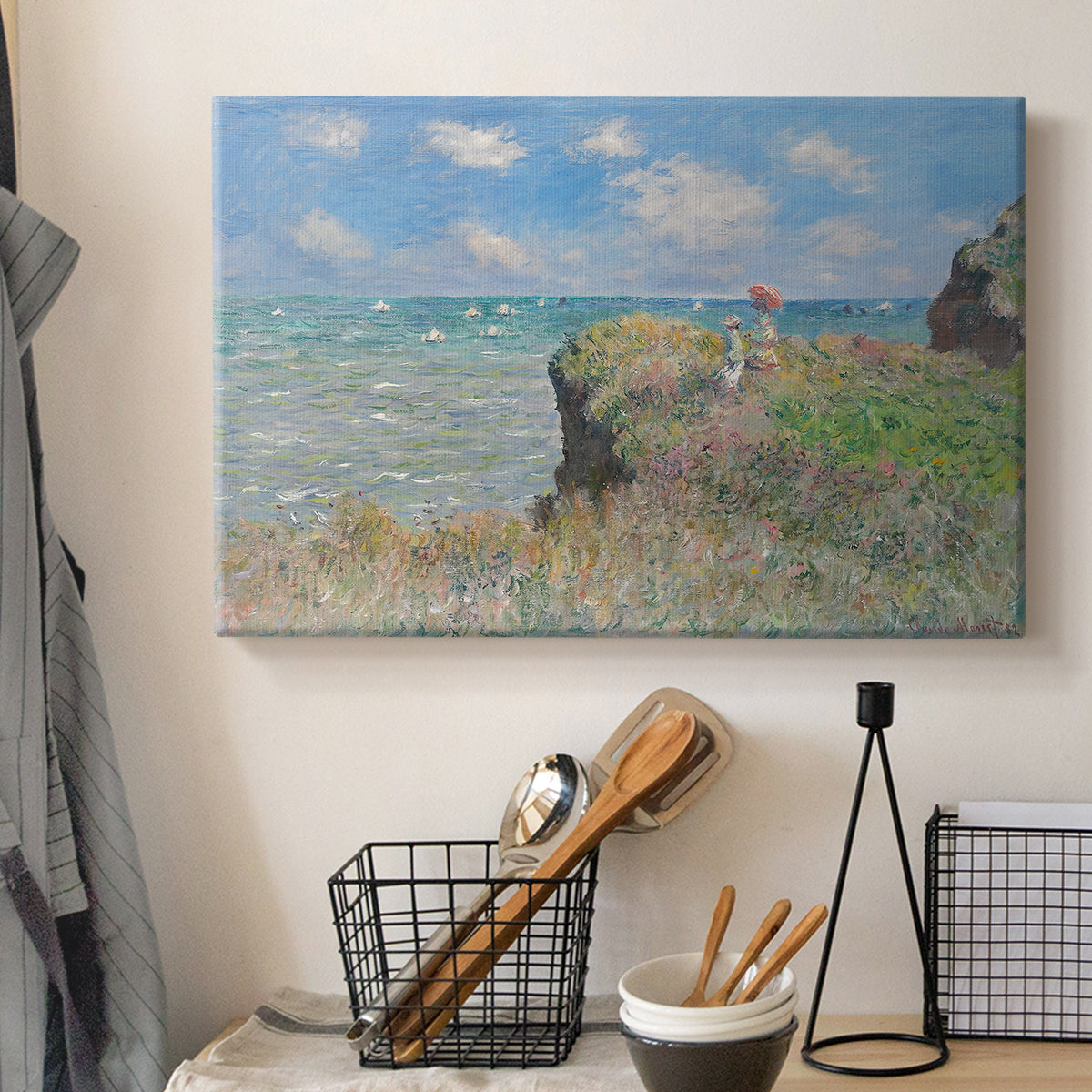 Canvas art print detailing an elevated shoreline path with figures and bright sky, displayed in a softly lit workspace setting