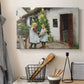 Canvas art print detailing a farmhouse exterior with figures engaged in everyday moment, displayed in a softly lit workspace setting