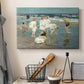 Canvas art print detailing a lively shoreline scene with people gathered in surf, displayed in a softly lit workspace setting