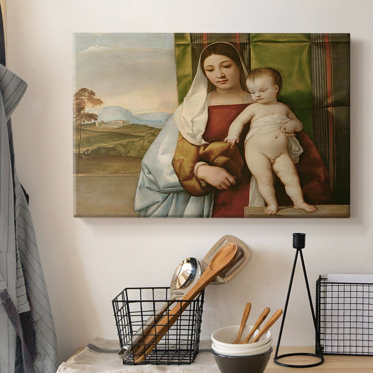 Canvas art print detailing a devotional image with seated woman and infant in quiet outdoor scene, displayed in a softly lit workspace setting
