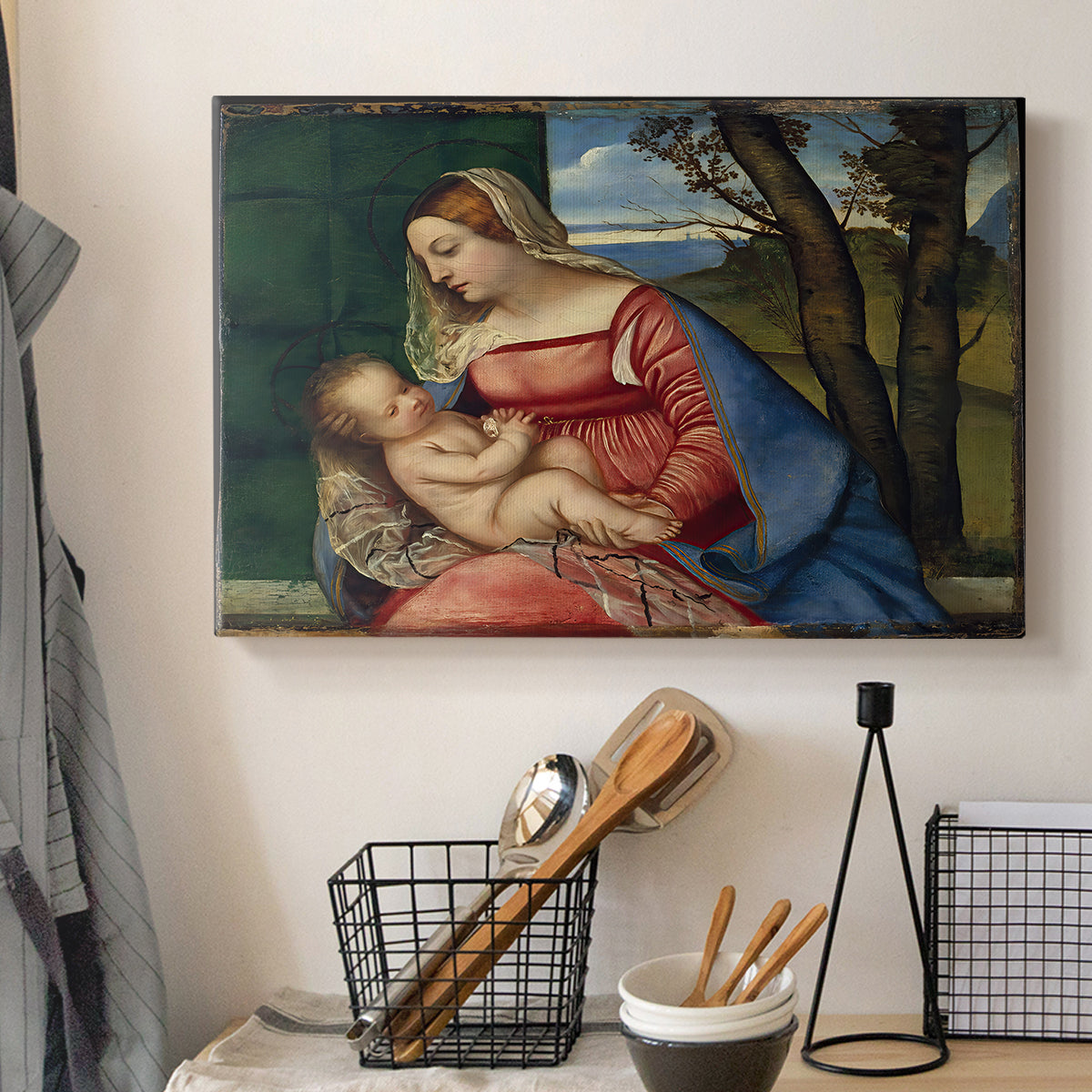 Canvas art print detailing a sacred figure study with child held against dark background, displayed in a softly lit workspace setting