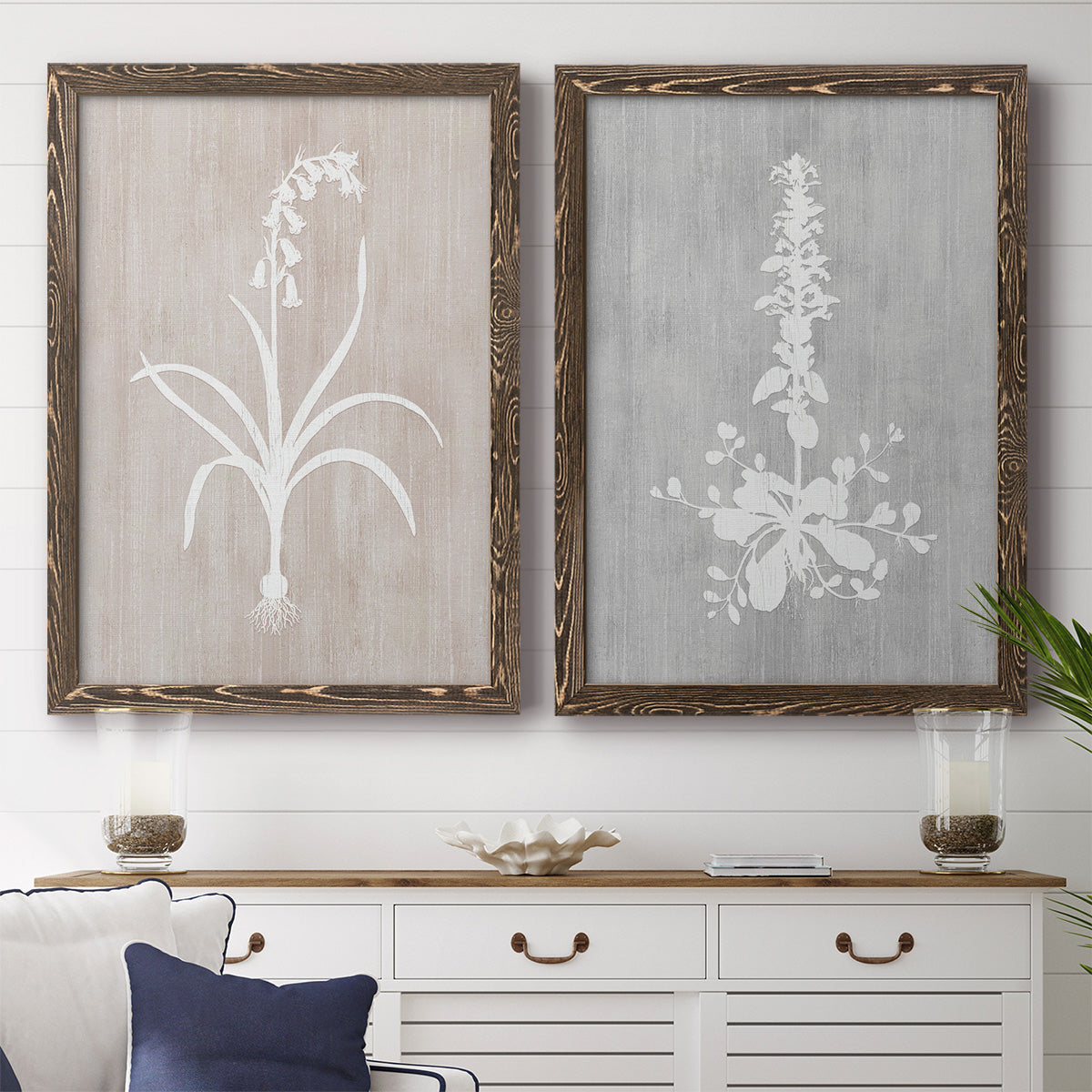 Set of two walnut barnwood framed canvas prints depicting a coordinated art pair of white botanical silhouettes on softly weathered neutral backgrounds rendered as rustic minimalist botanical prints above a dining room sideboard.
