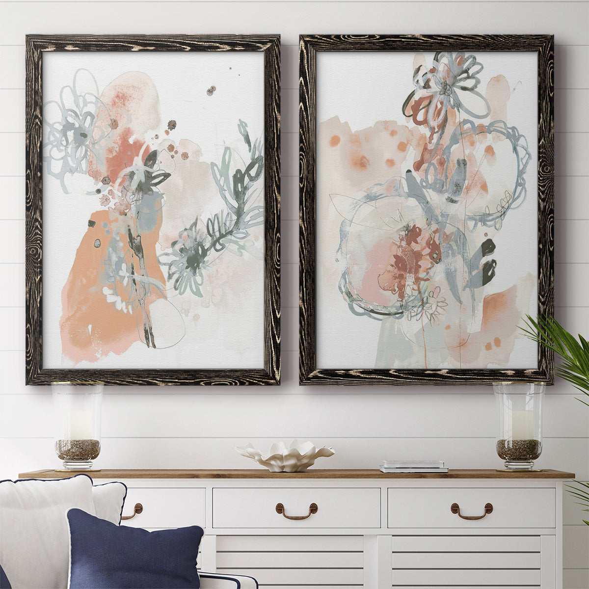 Set of two black barnwood framed canvas prints depicting a coordinated art pair of loose blush gray and coral floral gestures rendered as abstract watercolor botanicals above a dining room sideboard.