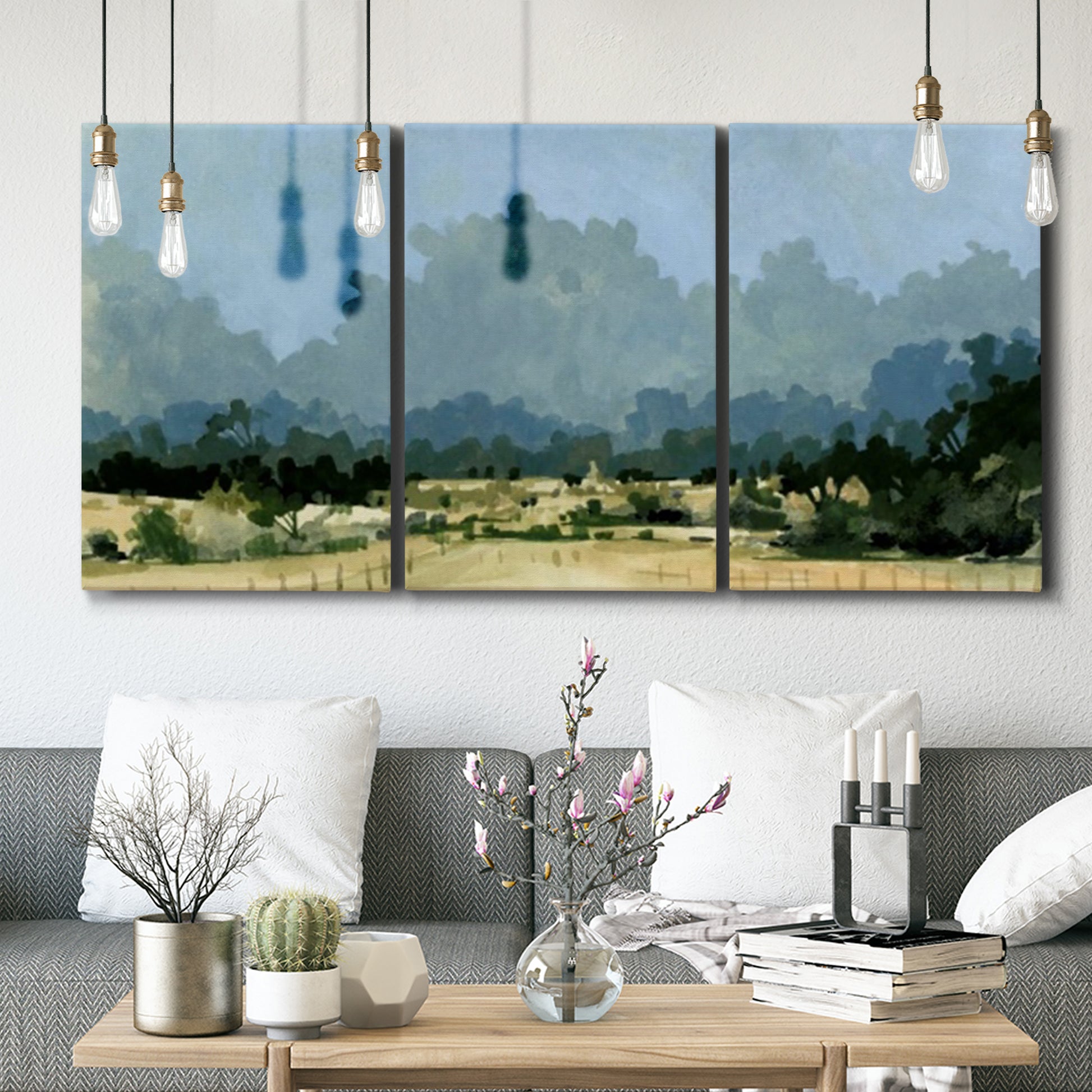 Three-panel canvas wall art featuring rural farmland landscape in watercolor, displayed in a modern living room above seating.