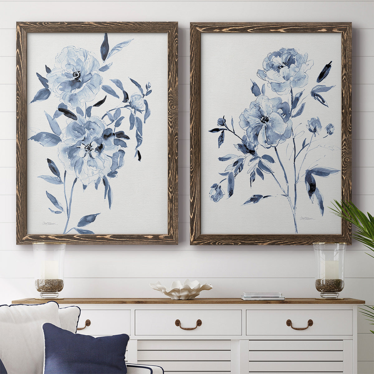 Set of two walnut barnwood framed canvas prints depicting a coordinated art pair of loose blue flowers and leafy branches rendered as expressive watercolor botanical paintings above a dining room sideboard.