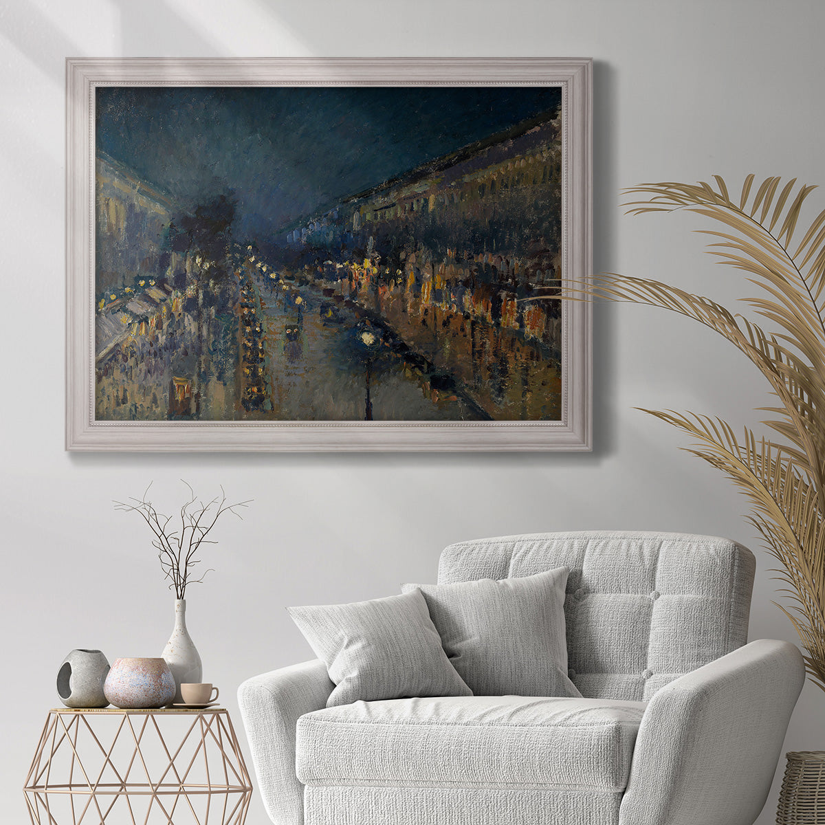 Impressionist nighttime Paris street scene by Camille Pissarro in an ornate weathered white frame displayed in a bright interior setting.