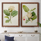 Set of two maple barnwood framed canvas prints depicting a coordinated art pair of white magnolia blossoms and glossy green leaves rendered as traditional botanical paintings above a dining room sideboard.