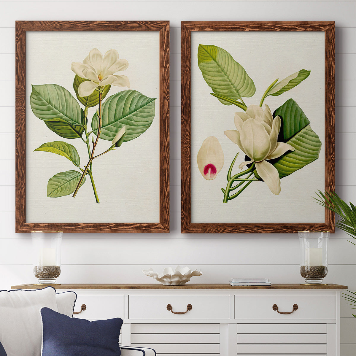 Set of two maple barnwood framed canvas prints depicting a coordinated art pair of white magnolia blossoms and glossy green leaves rendered as traditional botanical paintings above a dining room sideboard.
