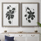 Set of two gray barnwood framed canvas prints depicting a coordinated art pair of black leafy vine silhouettes rendered as minimalist botanical prints above a dining room sideboard.