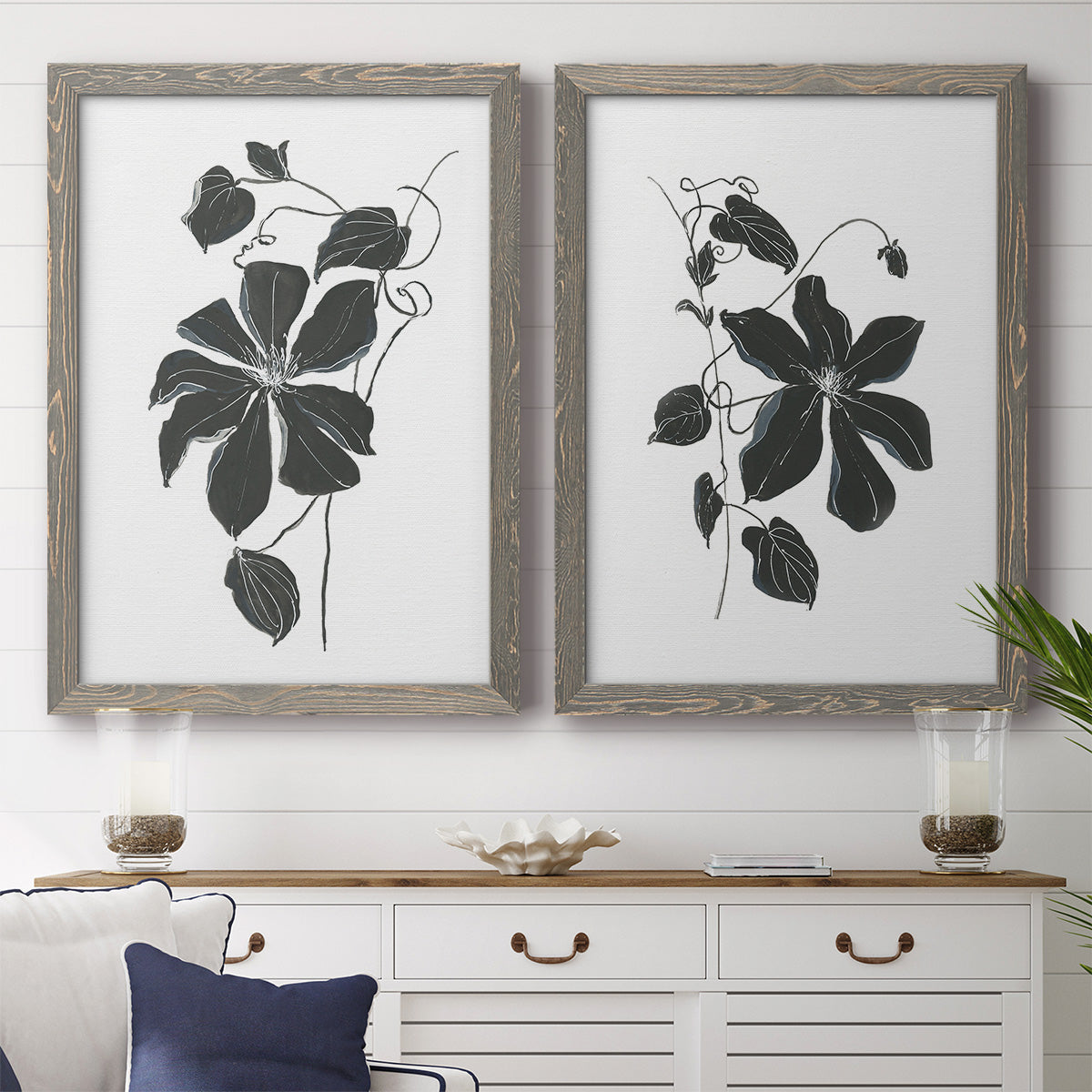 Set of two gray barnwood framed canvas prints depicting a coordinated art pair of black leafy vine silhouettes rendered as minimalist botanical prints above a dining room sideboard.