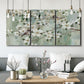 Three-panel canvas wall art featuring delicate spring blossoms with birds, displayed in a modern living room above seating.