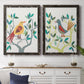 Set of two black barnwood framed canvas prints depicting a coordinated art pair of stylized colorful birds perched among leafy branches rendered as modern folk-art bird illustrations above a dining room sideboard.