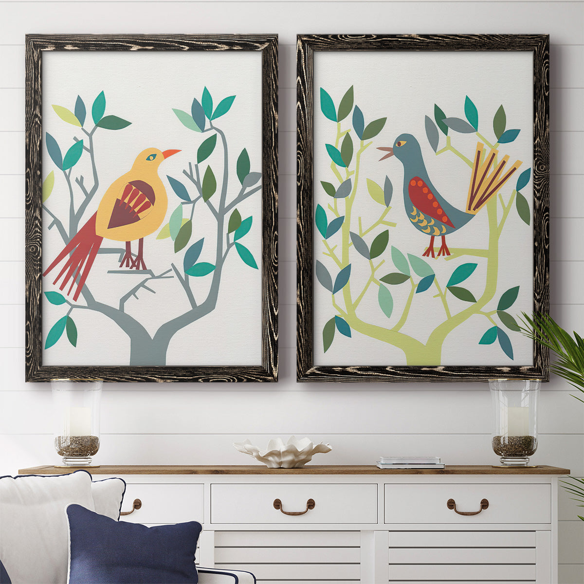 Set of two black barnwood framed canvas prints depicting a coordinated art pair of stylized colorful birds perched among leafy branches rendered as modern folk-art bird illustrations above a dining room sideboard.
