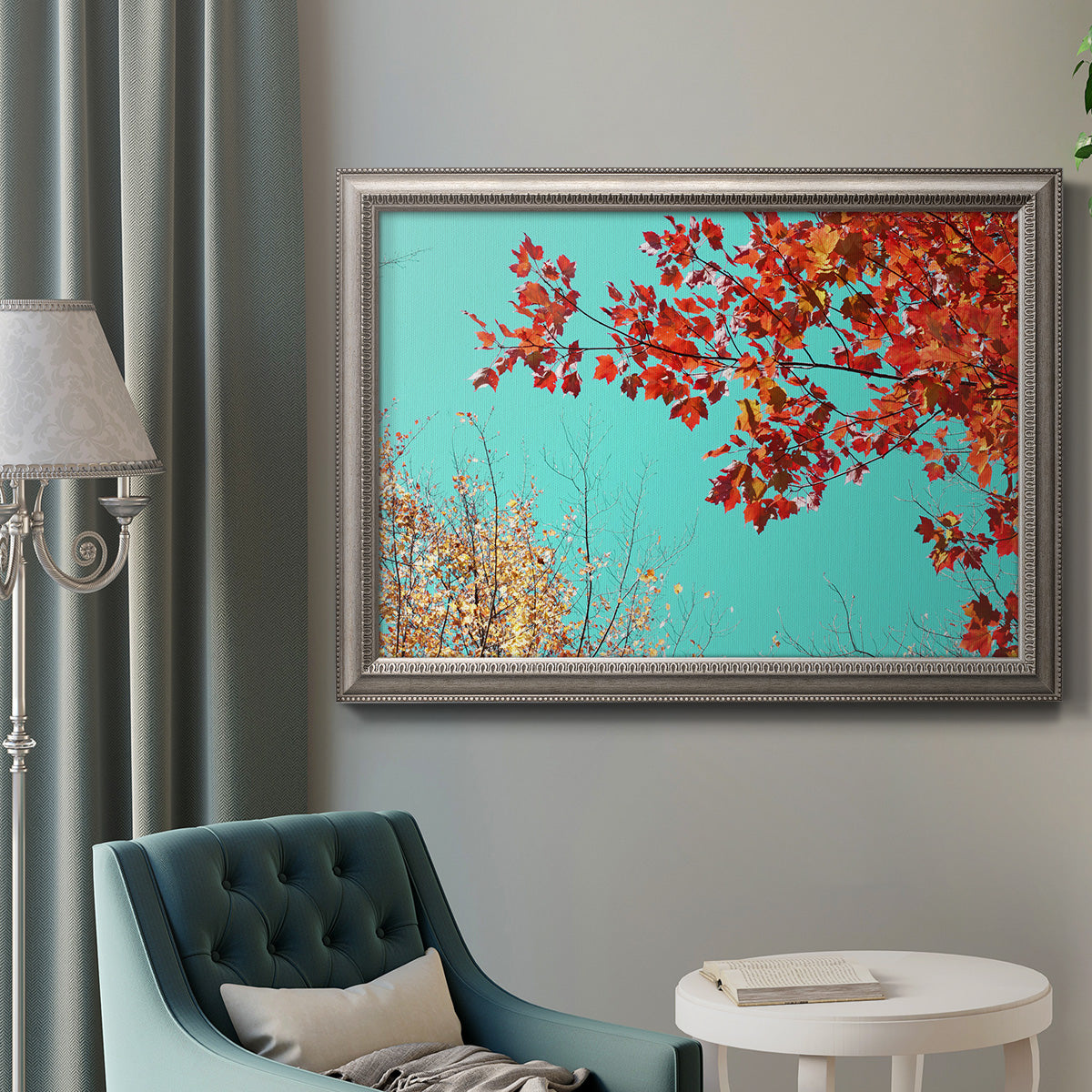 Red autumn leaves against a blue sky in an ornate vintage silver frame displayed in a neutral interior setting.